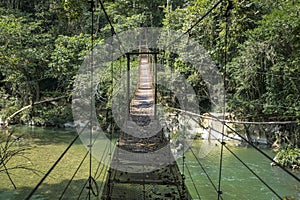 Hanging wooden bridge over Rio Claro Canyon in light and shadow, Doradal, Colombia