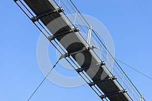 A hanging wooden bridge with steel ropes viewed from below against a blue sky.