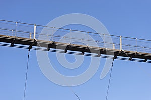 A hanging wooden bridge with steel ropes viewed from below against a blue sky.