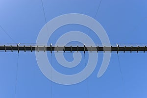 A hanging wooden bridge with steel ropes viewed from below against a blue sky.