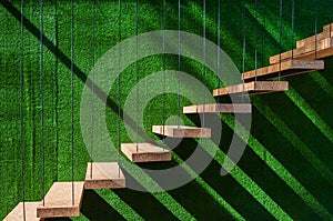 Hanging wooden stairs on artificial grass wall background Apartment staircase made of cables and wood apparently floating photo