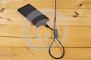 hangman noose made from an usb cable, connected to a generic smartphone, on wood boards background