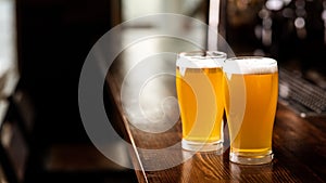 Hangouts with friends in pub and beer set. Two glasses of light beer with foam on wooden bar counter in daylight in