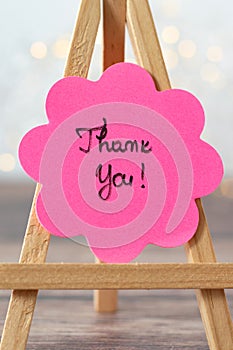 hank you text handwritten on pink sticky note in flower shape with bokeh background