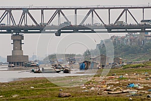 View to the bridge with intensive traffic and poor residential area below and garbage at the bank of the river in Hanoi, Vietnam.