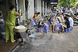 Hanoi, Vietnam - Sep 2, 2015: People eating Vietnamese traditional noodle soup Pho on sidewalk. Eating on pavement is common in Ha