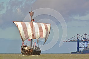 Hanseatic cog under sail with port facilities and cranes