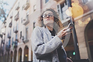 Hansome girl hipster wearing glasses searching information in mobile network by smart phone, during walk in european