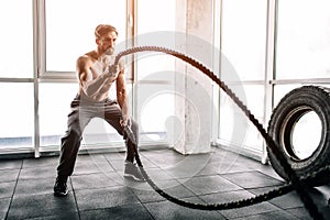 Hansome and well-built man is doing some exercises with waving two big and thick ropes one after another. This exercise