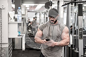 Hansome young athlete bearded man with headgear calling cell phone during sport workout in fitness gym listen music