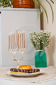 Hanukkah candlestick with all burning candles and donuts and a vase of flowers on the table.
