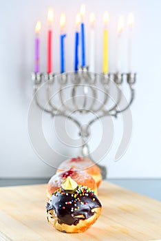 Hanukkah celebration concept. Close up view of tasty donuts with jam and menorah traditional candelabra.