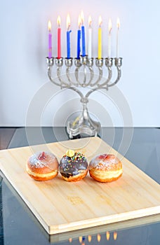 Hanukkah celebration concept. Close up view of tasty donuts with jam and menorah traditional candelabra.