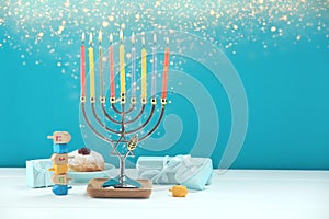 Hanukkah celebration. Menorah with burning candles, dreidels, gift boxes and donut on white wooden table against light blue