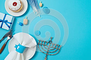 Hanukkah celebration table decoration with plate, stylish cutlery, gift box and traditional donuts on blue background. Top view,