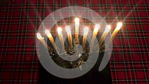 Hanukkah. Top view of a candle holder with burning candles. On the background of a red checkered tablecloth