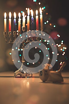Hanukkah traditional chandelier menorah burning candles and spinning top toys dreidels on the background of Christmas tree