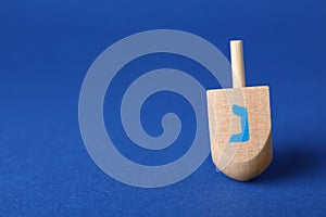 Hanukkah traditional dreidel with letter Nun on blue background, space for text