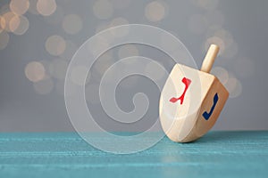 Hanukkah traditional dreidel with letters Gimel and Nun on wooden table against blurred lights. Space for text