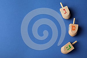 Hanukkah traditional dreidels with letters Gimel, Pe and He on blue background, flat lay. Space for text