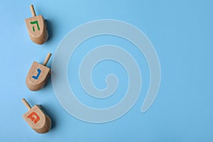 Hanukkah traditional dreidels with letters He, Pe and Nun on light blue background, flat lay. Space for text