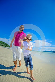 The happiest childhood: father and son running along the tropical beach