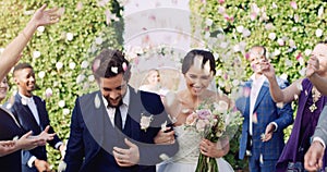 Happily ever afters do exist. an affectionate young newlywed couple leaving their wedding venue with their guests photo
