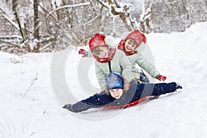 Sisters twins are sitting on the boy`s back and sledging