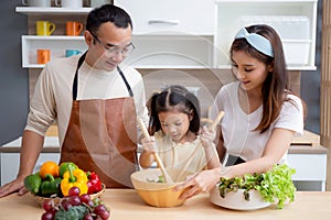Happiness asian family with father, mother and daughter preparing cooking salad vegetable food together.