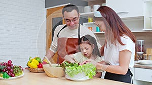 Happiness asian family with father, mother and daughter preparing cooking salad vegetable food together in kitchen.
