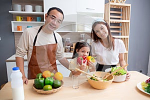 Happiness asian family with father, mother and daughter preparing cooking salad vegetable food together in kitchen.