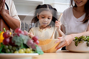 Happiness asian family with father, mother and daughter preparing cooking salad vegetable food together in kitchen.