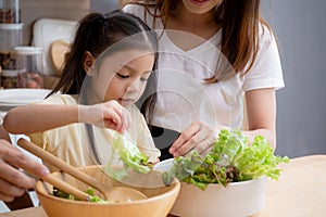 Happiness asian family with father, mother and daughter preparing cooking salad vegetable food together in kitchen.