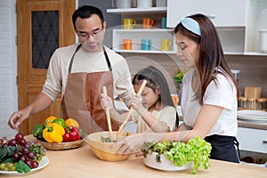 Happiness asian family with father, mother and daughter preparing cooking salad vegetable food together in kitchen.