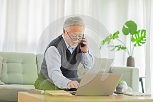 Happiness Asian senior handsome business man with white hairs hold mobile phone and using computer laptop talking with business