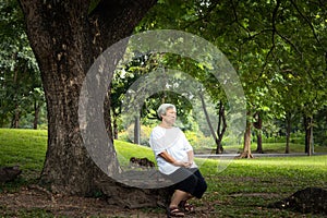 Happiness asian senior woman very calm in green nature at park,relax time,concentrate elderly people sit under the tree, feel photo