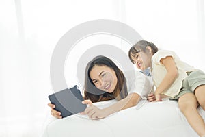 Happiness Asian young mother and little cute daughter lying on bed in the house use labtop for entertain, family joyful together