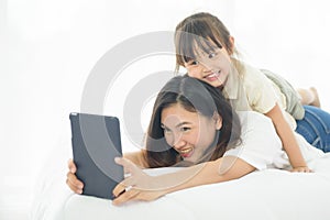 Happiness Asian young mother and little cute daughter lying on bed in the house using labtop for entertain