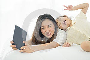 Happiness Asian young mother and little cute daughter lying on bed in the house using laptop for take photo