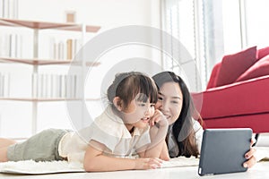 Happiness Asian young mother and little cute daughter lying on floor of house using labtop for entertain