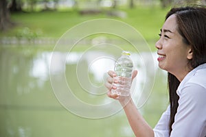 Happiness Beautiful asian chinese women holding mineral water bottle. Young Woman Drinking Water from bottle in green garden Park