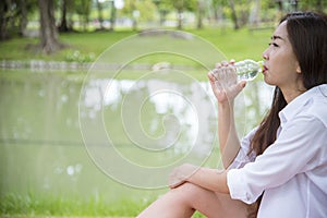 Happiness Beautiful asian chinese women holding mineral water bottle. Young Woman Drinking Water from bottle in green garden Park