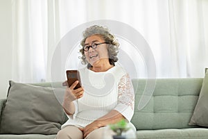 Happiness beautiful elderly asian woman with white hairs sitting on sofa using mobile phone and social media smile at home,Senior