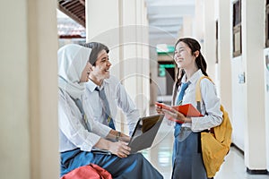 happiness a boy, girl, and girl in a veil in high school uniform using a laptop computer together when discussing