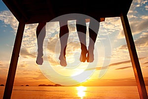 Happiness concept, silhouette of feet of couple sitting on the pier on beach