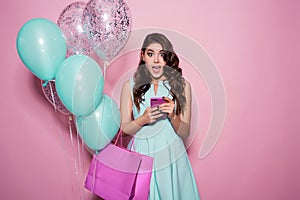 Happiness, consumerism, sale and people concept - smiling young woman with shopping bag and balloons over pink