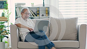 Happiness elderly asian man sitting on sofa and using computer laptop and smile at home,Senior lifestyle at home concept