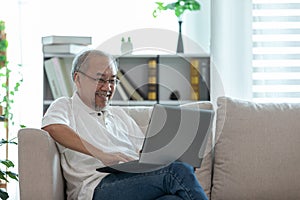 Happiness elderly asian man sitting on sofa and using computer laptop and smile at home,Senior lifestyle at home concept