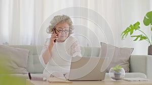 Happiness Elderly asian woman with white hairs talking with family on mobile phone and work with computer laptop in cozy living