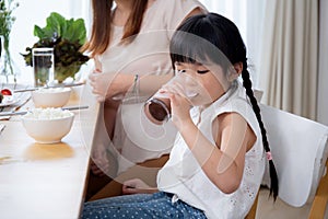 Happiness family with mother and adorable daughter drinking milk or beverage together in the living room.